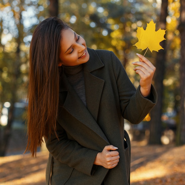 晴れた日に公園を散歩黄色い紅葉とファッショナブルなコートを着た笑顔で幸せな若い美しい女性