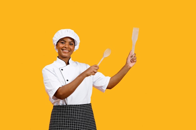 Happy young black chef lady pointing at copy space with wooden spatulas