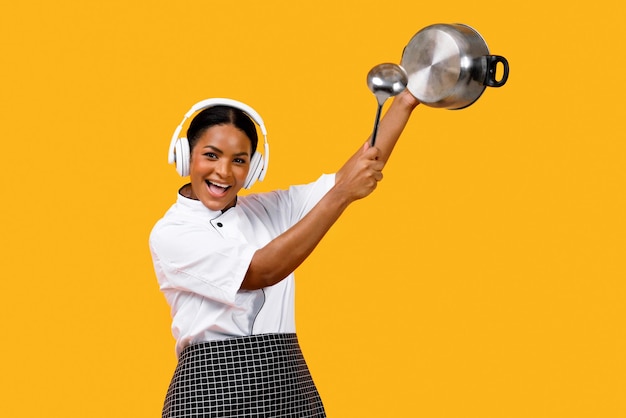 Happy young black chef woman in headphones having fun while cooking