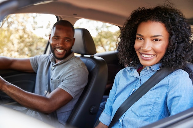 Happy young black couple driving in a car smiling to camera