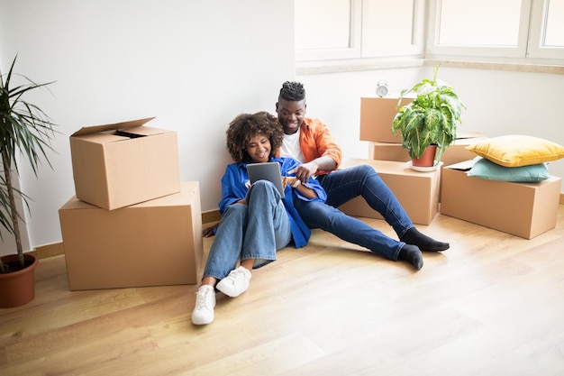 Happy young black couple ordering online with digital tablet after moving home