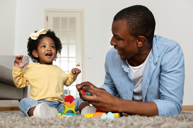 Happy young black father playing together with little baby daughter