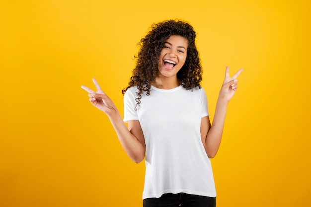 Happy young black girl showing peace gesture isolated over yellow