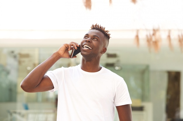 Happy young black guy standing outdoors and making a phone call