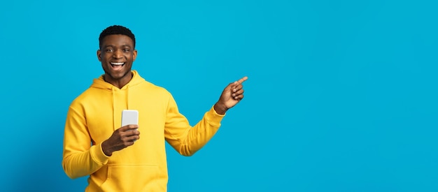 Happy young black guy in yellow hoodie using smartphone panorama