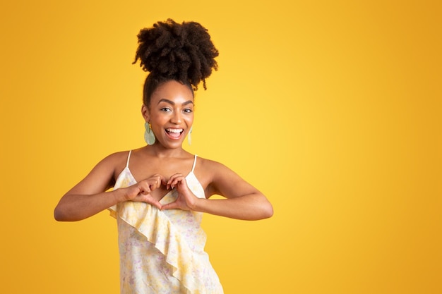 Happy young black lady in dress making heart sign with hands