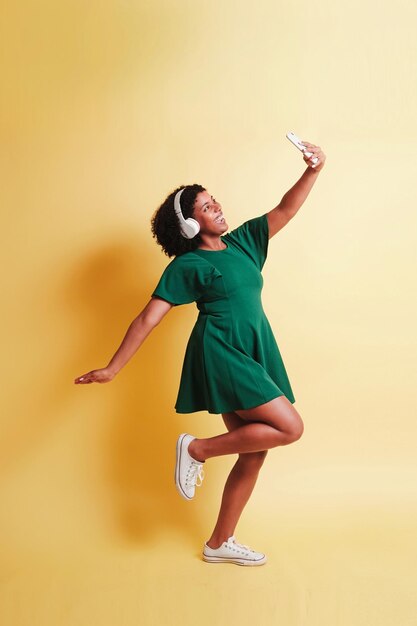 Foto giovane donna nera felice con un telefono cellulare con le cuffie che scattano un selfie