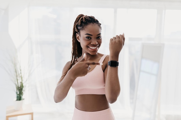 Happy young black woman pointing at activity fitness tracker with mockup having break in her