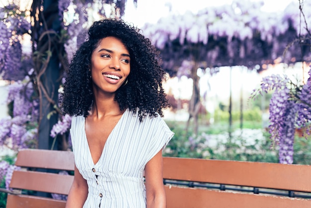 Happy young black woman sitting surrounded by flowers