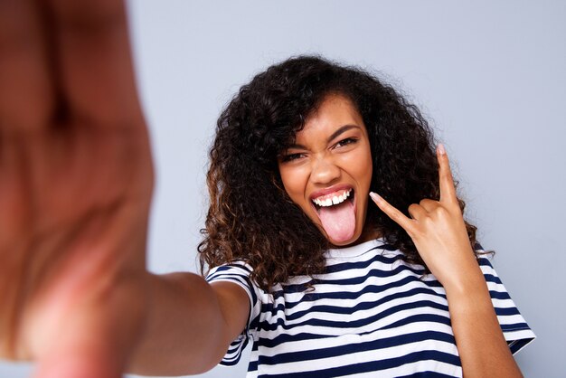 Giovane donna di colore felice che prende selfie contro la parete grigia