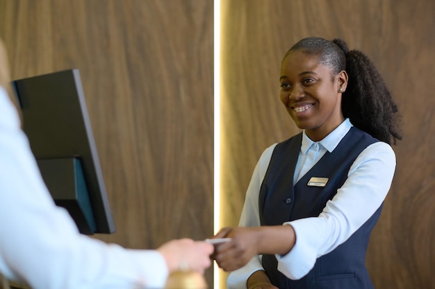 Happy young black woman in uniform passing passport to male traveler