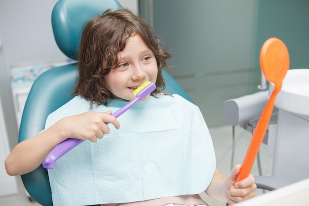 Happy young boy brushing teeth with huge toothbrush at dentists office