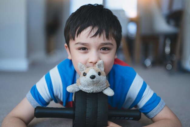 Happy young boy lying on floor playing with dog toy Kid with smiling face playing alone at home on weekend Positive Child relaxing at home in the morning