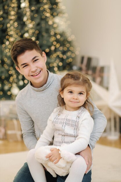 姪と一緒に幸せな少年がモミの木のクリスマス気分の前で遊ぶ