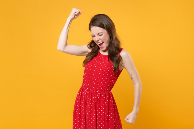 Happy young brunette woman girl in red summer dress posing isolated on yellow wall background studio