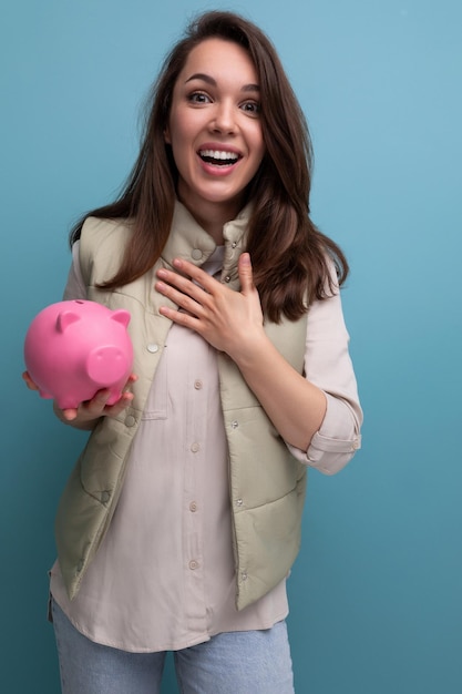 Happy young brunette woman holding pink piggy bank money