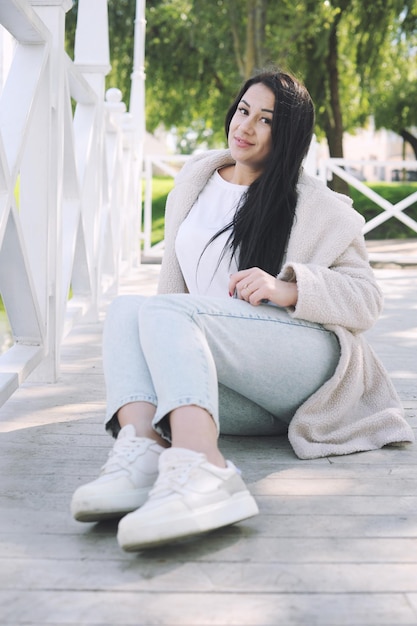 Happy young brunette woman outdoor dressed in faux white fur coat and jeans