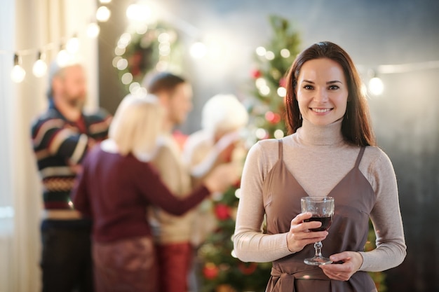 Happy young brunette woman with glass of wine congratulating you on merry Christmas with her family