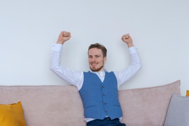 幸せな若いビジネスマンは、空中に手を上げてソファに座っています