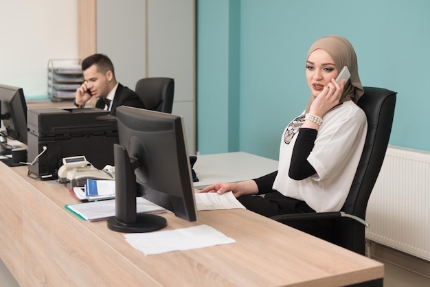 幸せな若いビジネスマンとイスラム教徒の女性は、コンピューターの近代的なオフィスで働いています
