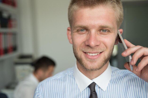 Foto felice giovane uomo d'affari parlando al telefono in ufficio moderno dietro di lui seduto il suo collega