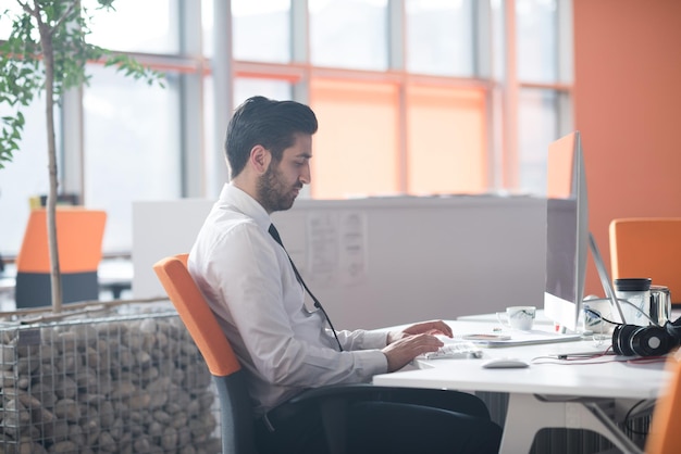 happy young business man  working on desktop computer at his desk in modern bright startup office interior