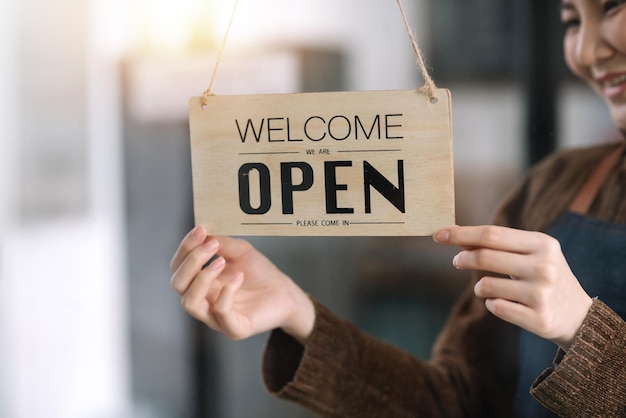 Happy young business owner standing with holding open sign board