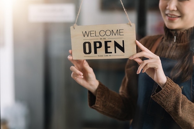 Happy young business owner standing with holding open sign board