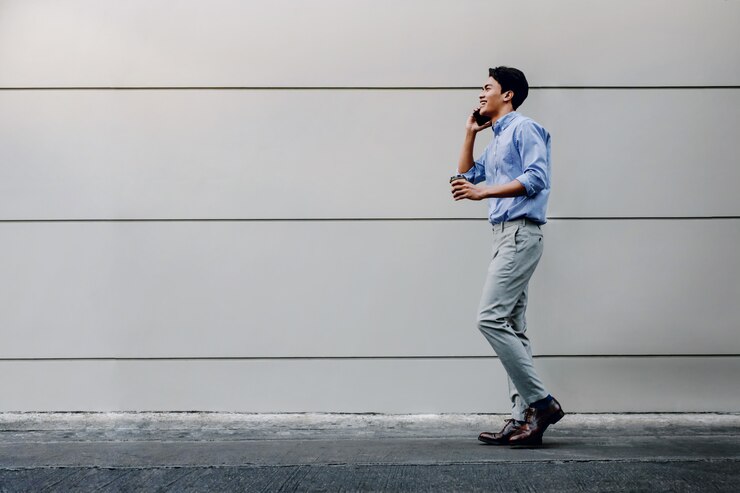 Photo happy young businessman in casual wear using mobile phone while walking by the urban building wall. lifestyle of modern people.