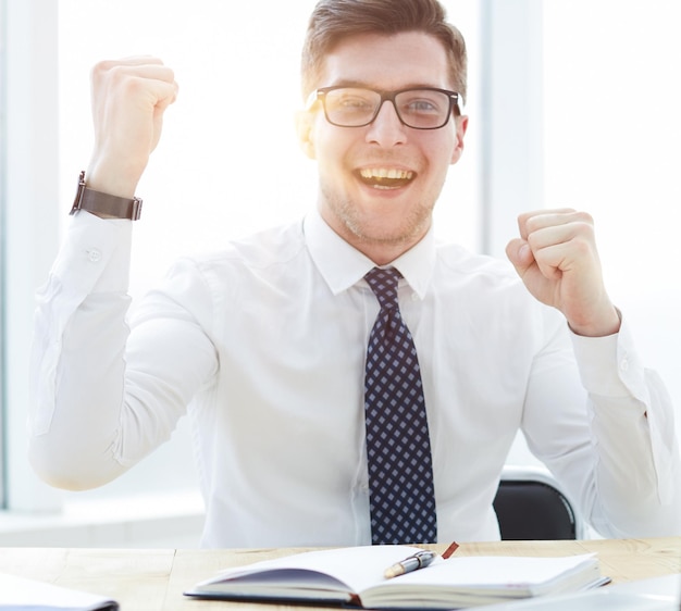 Foto felice giovane uomo d'affari che alza le mani davanti al computer portatile alla scrivania dell'ufficio