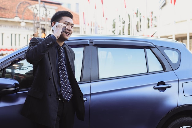 Happy young businessman talking on the phone while standing near his car outdoors