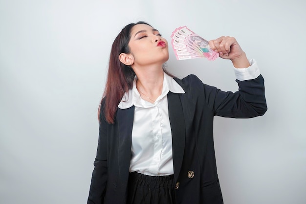 A happy young businesswoman is wearing black suit and holding cash money in Indonesian rupiah isolated by white background