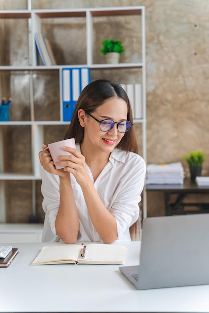 Felice giovane imprenditrice utilizzando il computer portatile facendo shopping online sorridente bella donna asiatica seduta e lavorando sul posto di lavoro