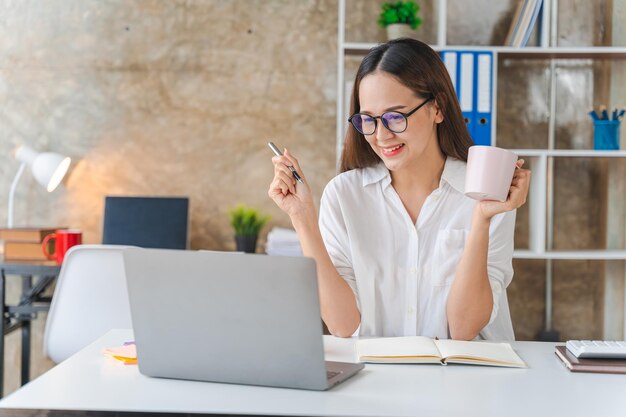 Happy young businesswoman using laptop computer doing online shopping Smiling beautiful Asian woman sitting and working at workplace