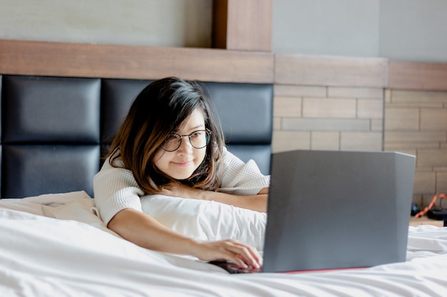 Happy young businesswoman wear glasses working on laptop in bedroom in morning  