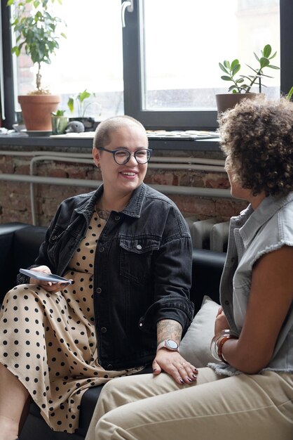 Happy young businesswoman with mobile phone talking to her biracial colleague