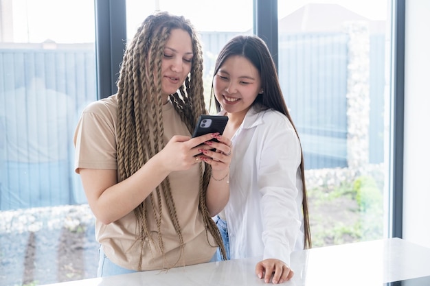 Happy young carefree diversity women friends in casual using phone having fun together at home