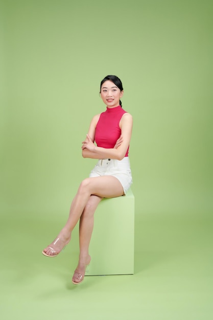 Photo happy young casual woman sitting on a box stool with hands crossed on green background