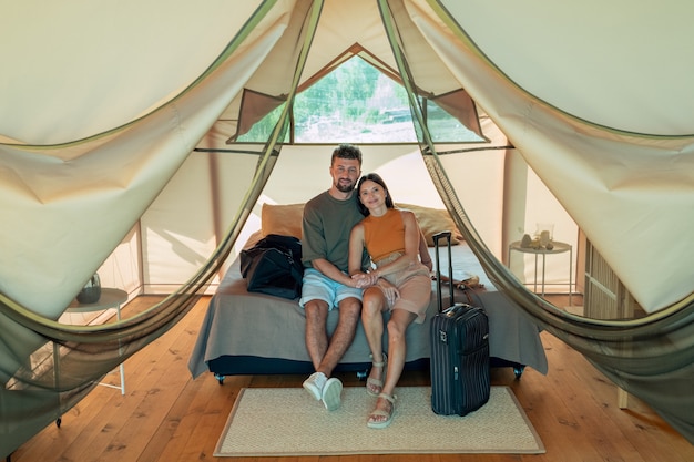 Happy young caucasian couple relaxing on bed inside glamping house