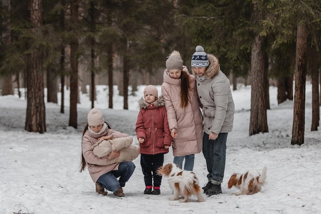 Happy young caucasian family plays with a dog in winter in a pine forest