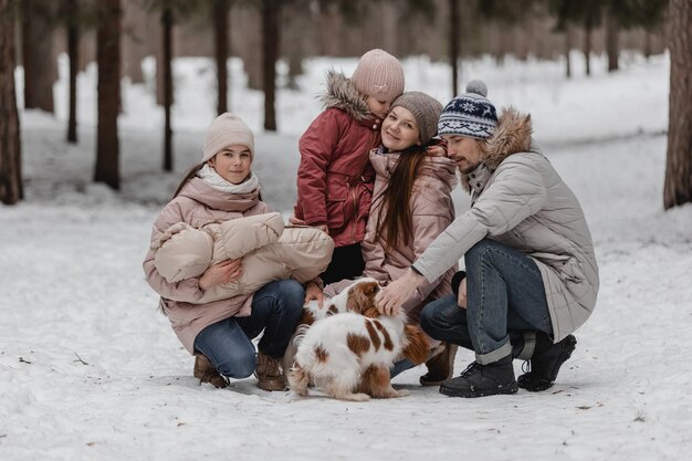 Happy young caucasian family plays with a dog in winter in a pine forest