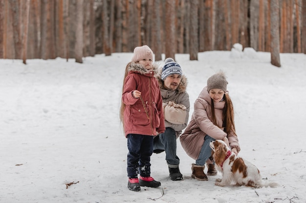 Happy young caucasian family plays with a dog in winter in a pine forest