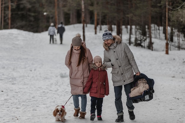 Happy young caucasian family plays with a dog in winter in a pine forest