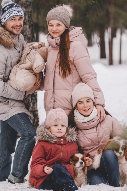 Happy young caucasian family plays with two dogs in winter in a pine forest The concept of Christmas and New Year