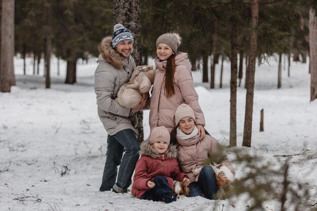 Happy young caucasian family plays with two dogs in winter in a pine forest