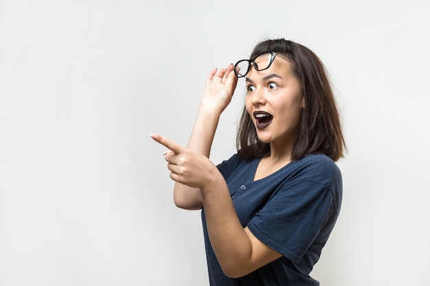 Happy young caucasian female in a blue shirt with glasses pointing fingers away