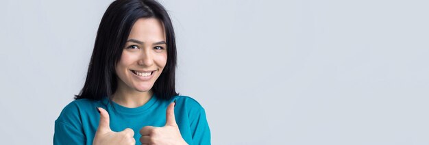 親指を立てるサインと笑顔を作る青いTシャツで幸せな若い白人女性良い仕事