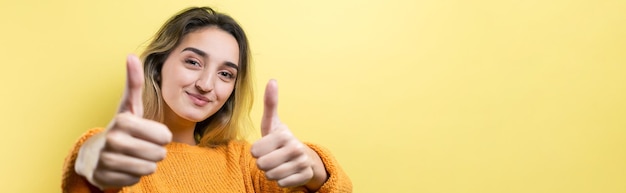 Счастливая молодая кавказская женщина в оранжевом свитере делает большой палец вверх и улыбается Хорошая работа и уважениеx9