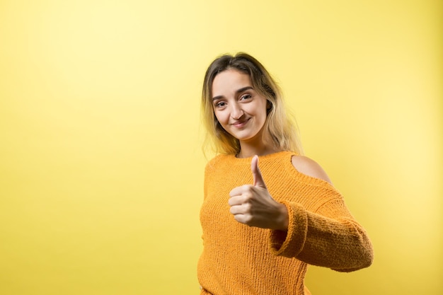 Felice giovane donna caucasica in un maglione arancione che fa segno con il pollice e sorridente buon lavoro e rispettox9