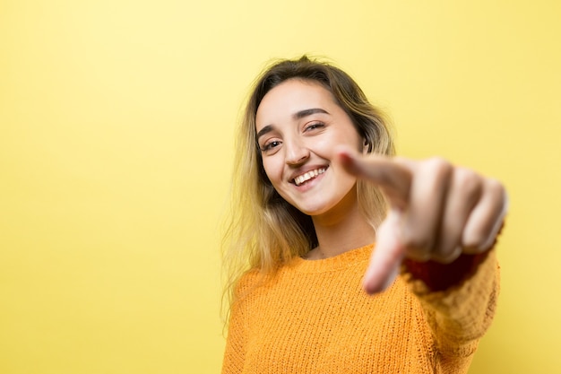 손가락을 멀리 가리키는 주황색 스웨터를 입은 행복한 젊은 백인 여성